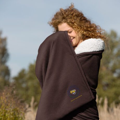 A woman is wrapped in a Premium Sherpa blanket in a field.