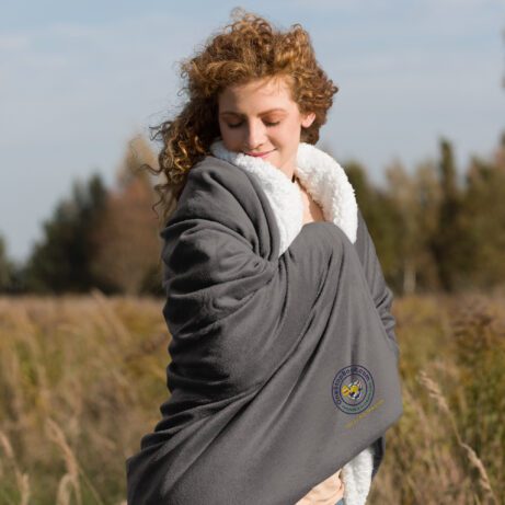 A woman is standing in a field wrapped in a Premium Sherpa Blanket.