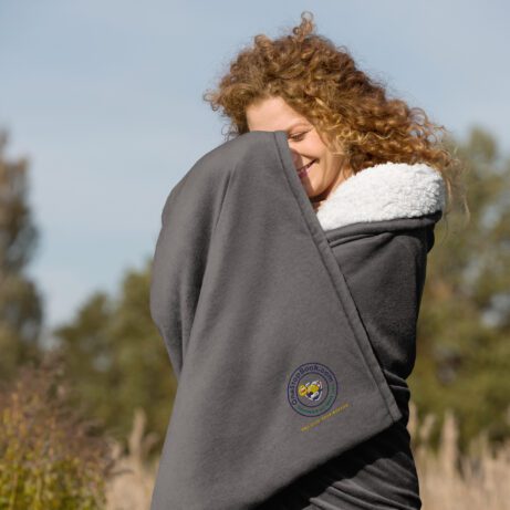 A woman is cozily wrapped up in a premium sherpa blanket in a field.
