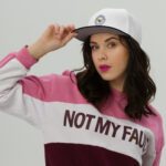 A woman wearing a sweatshirt with a Snapback Hat that says not my fault.