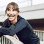 A smiling woman in stylish online workout clothes leaning on a railing.