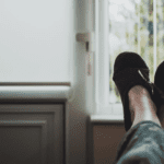 A person's feet in a pair of slippers in front of a window.